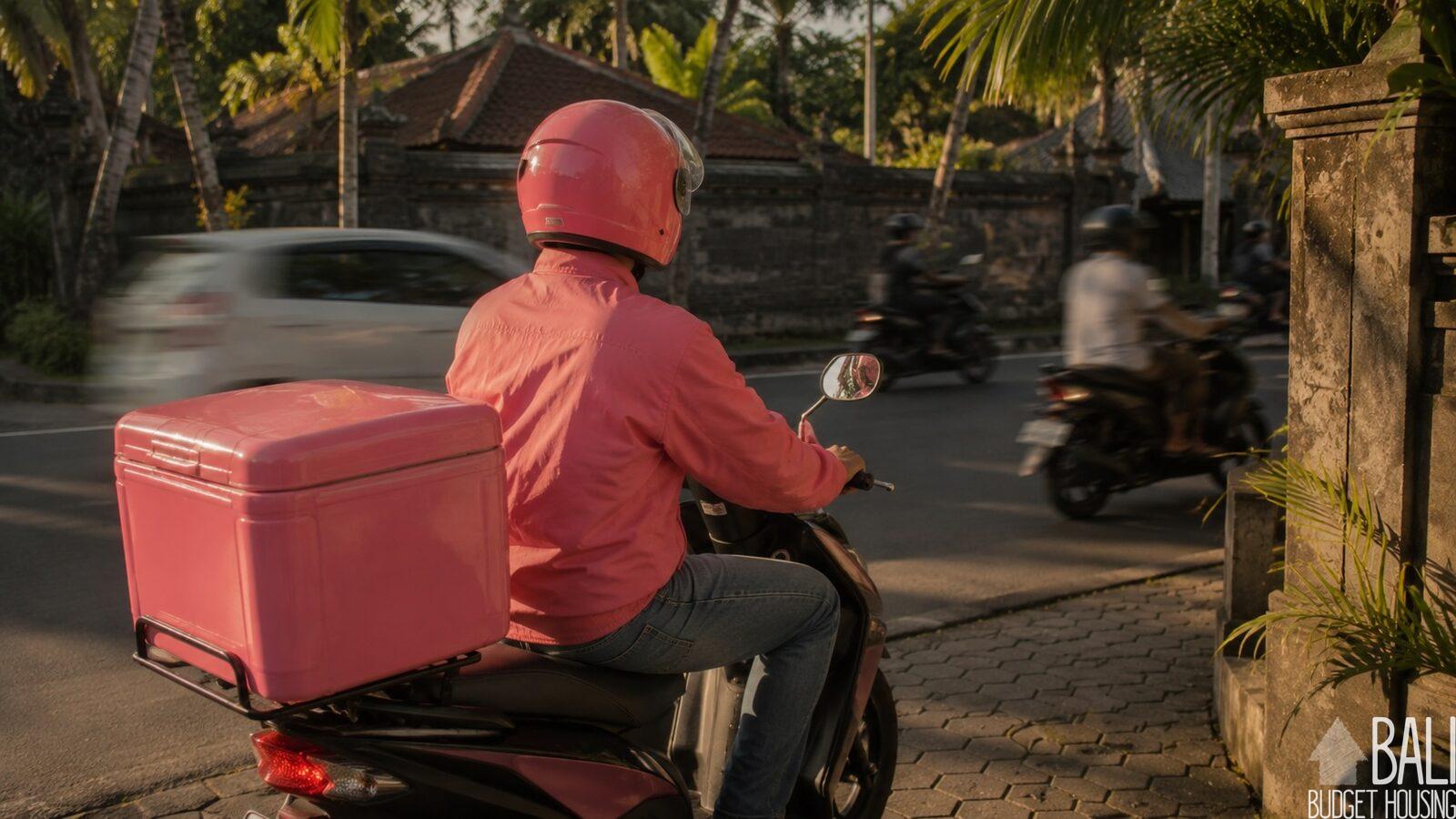 A food delivery rider on a scooter waiting on a street in Bali