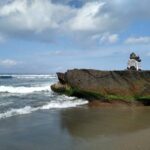 A Balinese shrine on a large rock at a beach in Canggu, with surf behind