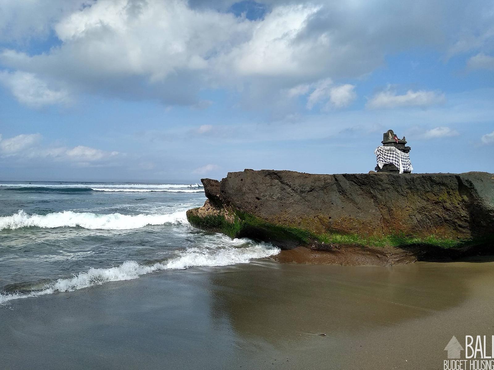 A Balinese shrine on a large rock at a beach in Canggu, with surf behind